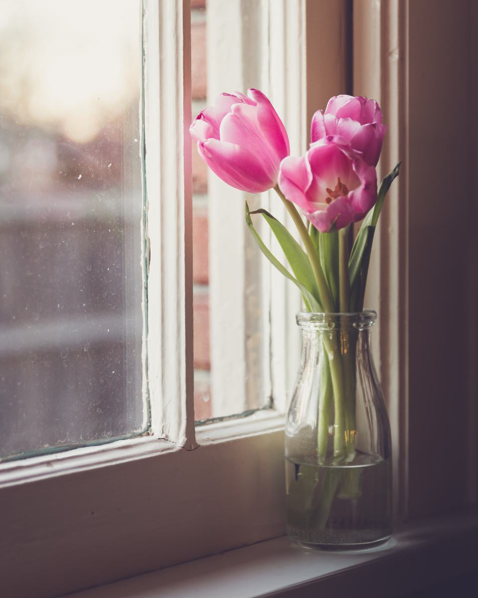 Roze tulpen in een glazen vaas op een vensterbank